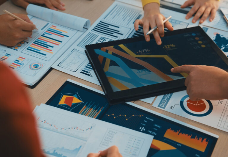 A diverse business team engages in collaborative work, analyzing charts and reports while using a digital tablet to drive strategic decisions in a modern office setting. SACTR